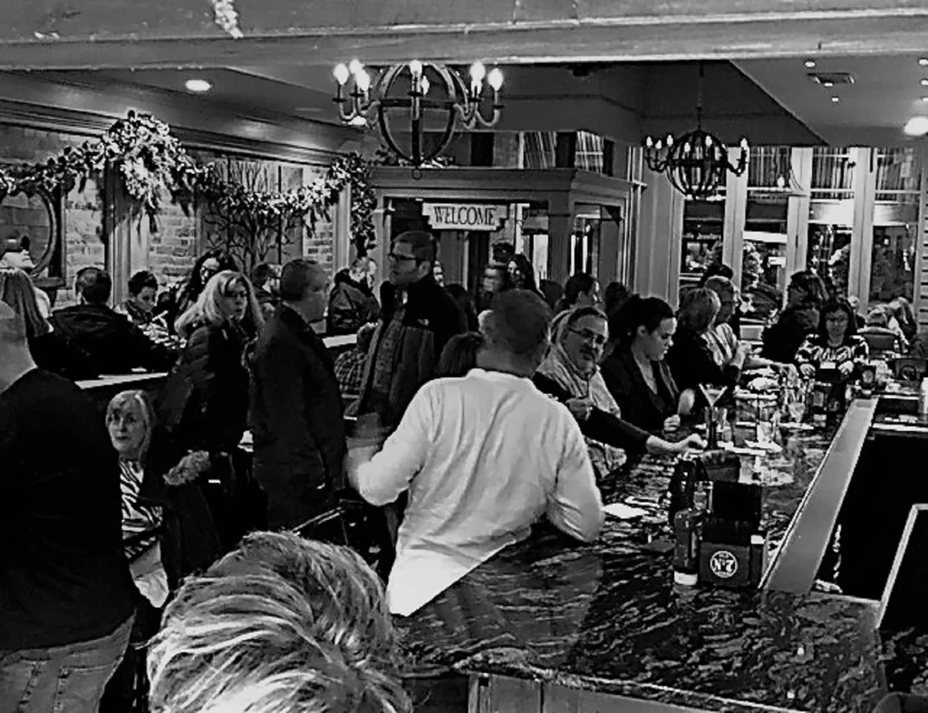 Black and white photo of a lively, crowded bar interior.