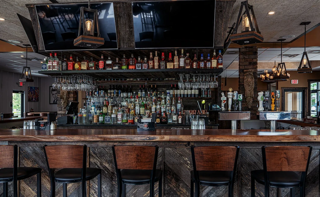Polished wooden bar with liquor bottles, beer taps, and empty stools.