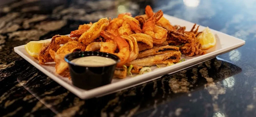 Piled plate of various crispy fried seafood, lemon, and dipping sauce.