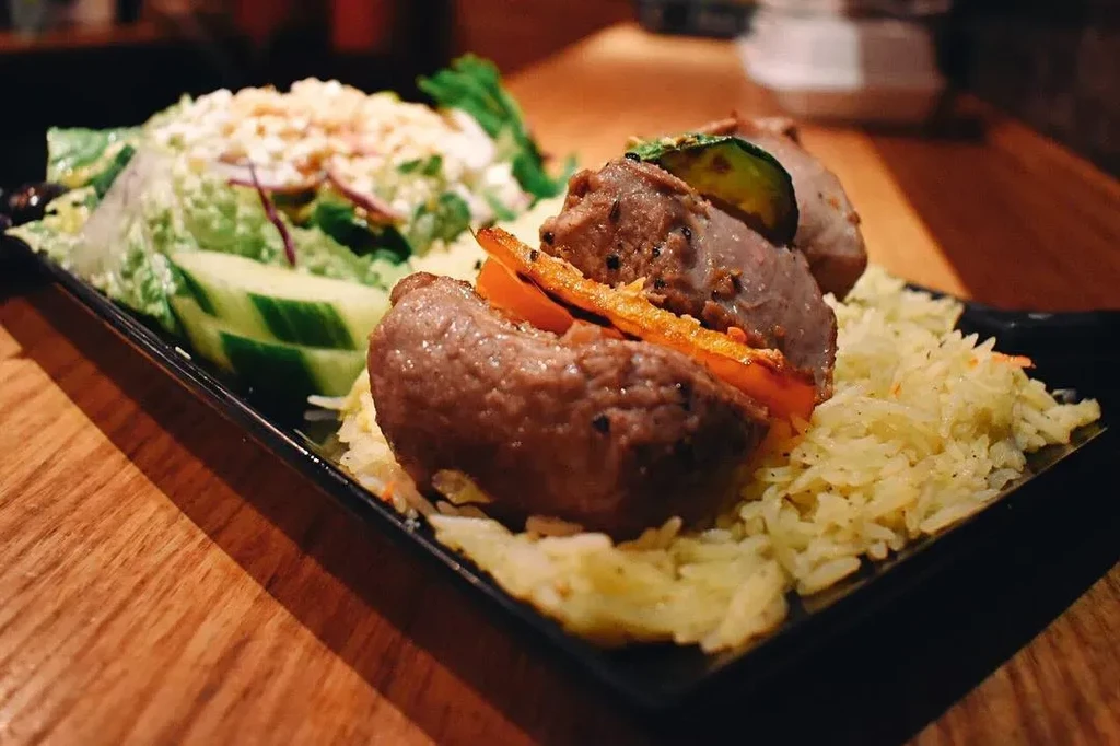Grilled meat, rice, vegetables, and salad on a black rectangular plate.