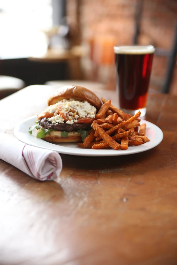 Gourmet burger with feta, arugula, sweet potato fries, and beer.