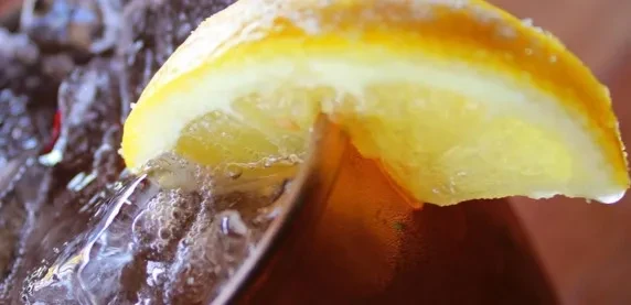 Close-up of a glass with a dark drink, ice, and lemon slice.