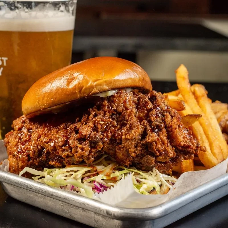 Crispy fried chicken sandwich, french fries, and beer on a metal tray.