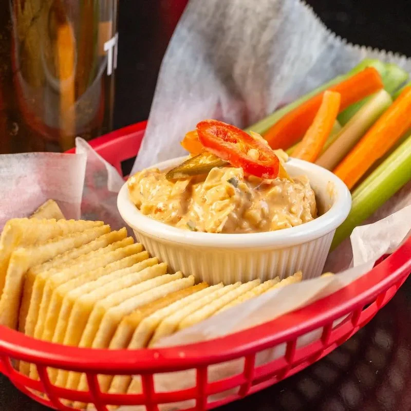 Creamy orange dip with peppers, carrots, celery, and crackers in basket.