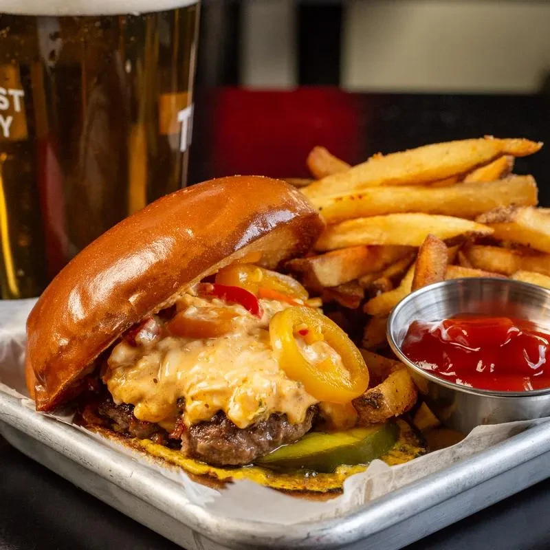 Gourmet burger, rustic fries, ketchup, and beer on a metal tray.