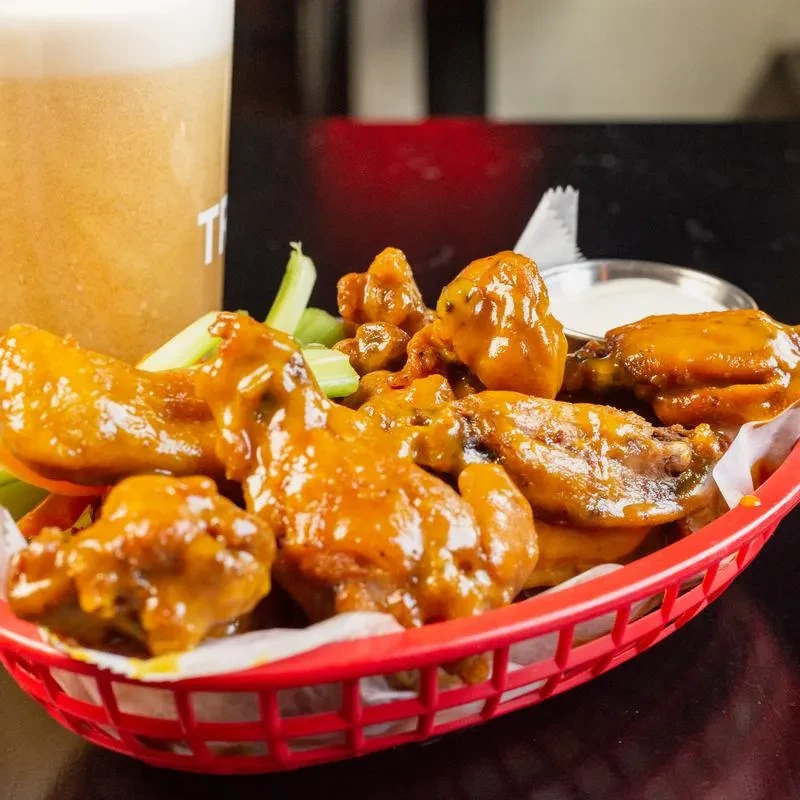 Orange-red chicken wings, celery, and dipping sauce in a red basket.