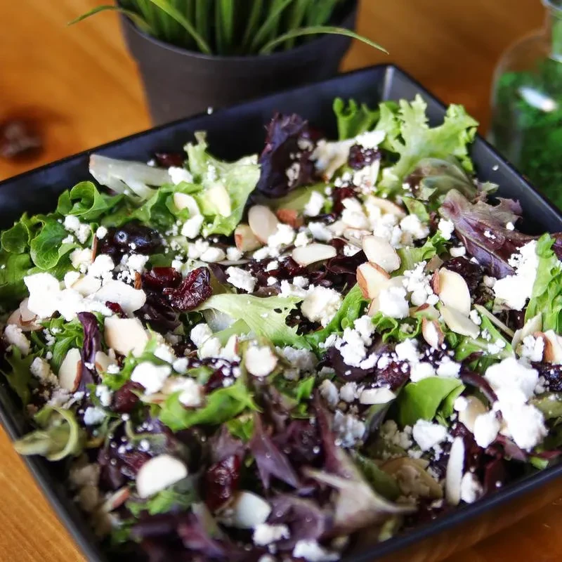 Close-up, overhead salad with mixed greens, white cheese, cranberries, almonds.