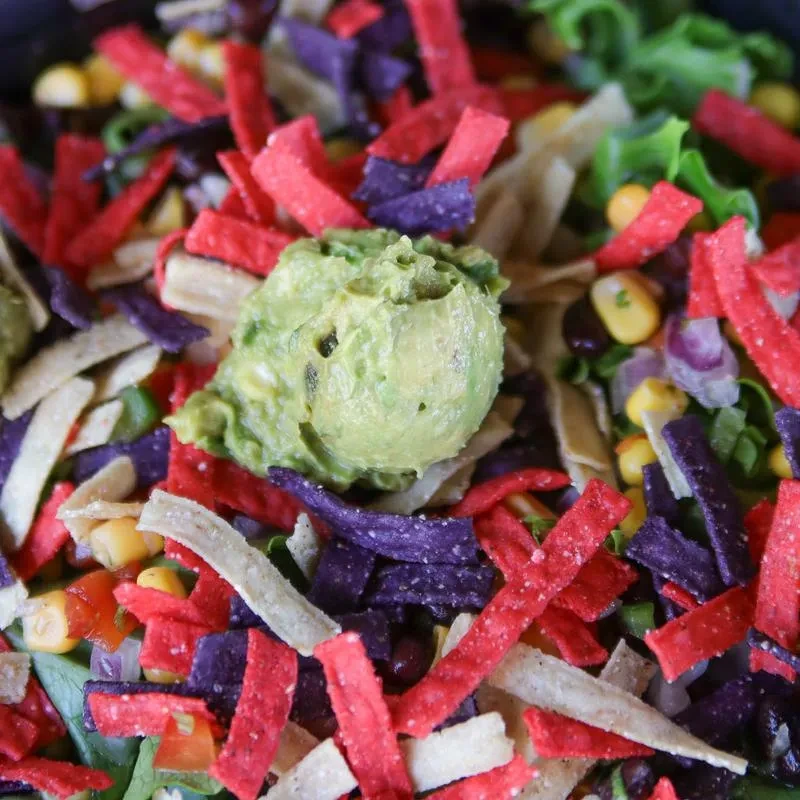 Colorful Mexican-inspired salad with guacamole, crispy tortilla strips, corn, and beans.