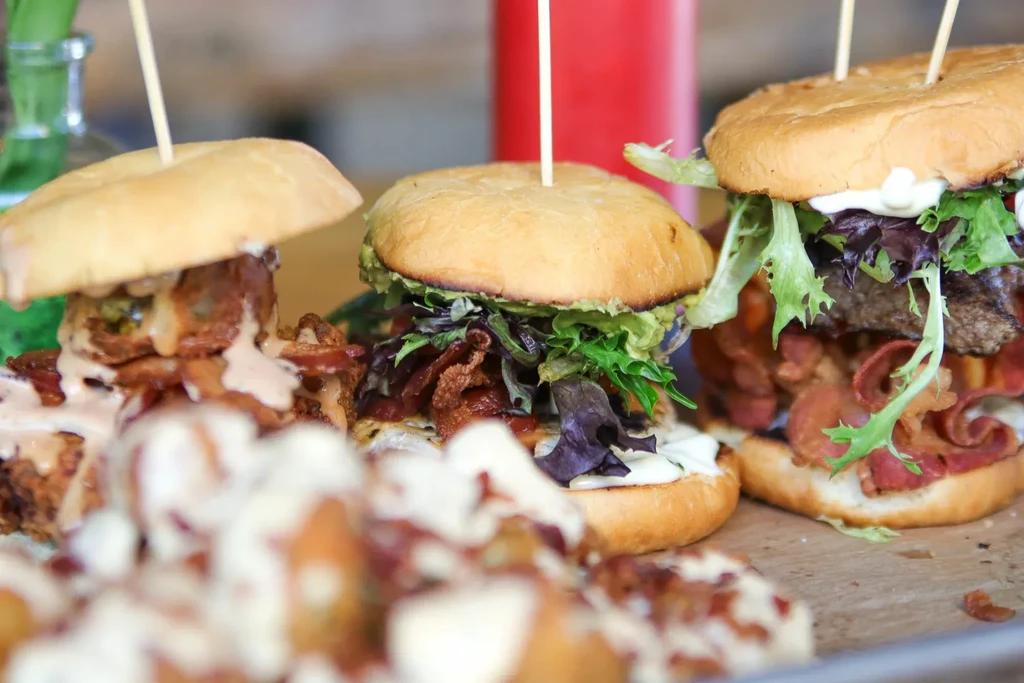 Three loaded gourmet burgers with bacon and lettuce on a rustic tray.