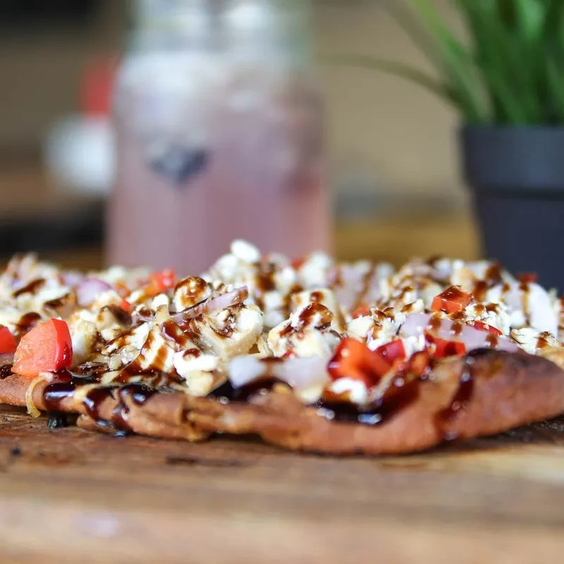 Savory flatbread topped with cheese, red onion, pepper, and dark glaze.
