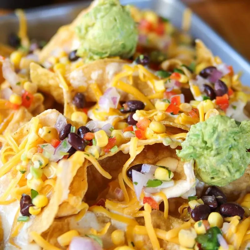 Loaded nachos with melted yellow cheese, salsa, guacamole, sour cream.