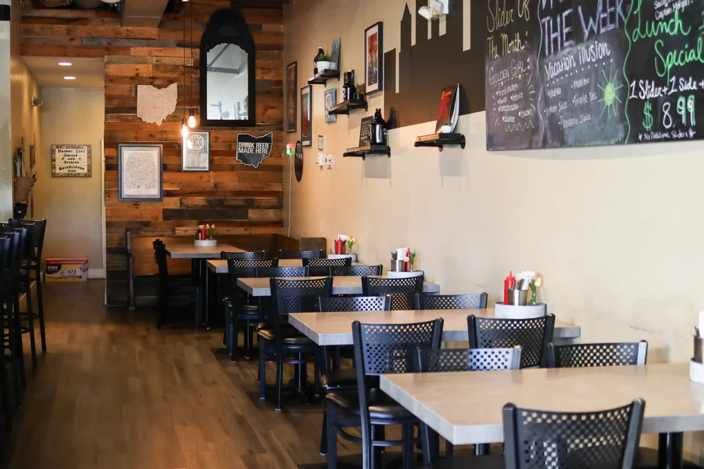Empty casual restaurant interior with industrial chairs, a rustic wood wall, and chalkboard menu.