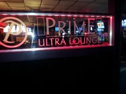 Nighttime view of "PRIME ULTRA LOUNGE" red neon sign and blurred interior.