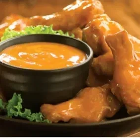 Close-up of glazed chicken wings, creamy orange dip, and lettuce.