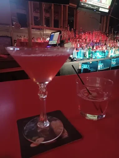 Two drinks on a bar counter, colorful backlit bottles, and a TV.