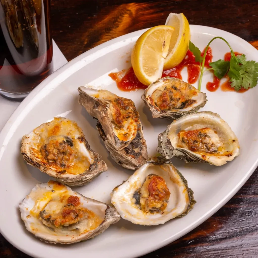 Six baked oysters with golden topping, lemon, red sauce, and cilantro.