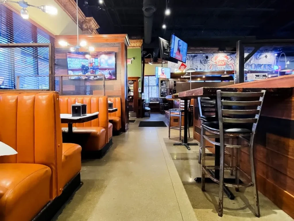 Sports bar interior featuring orange booths, a rustic bar, and TVs.