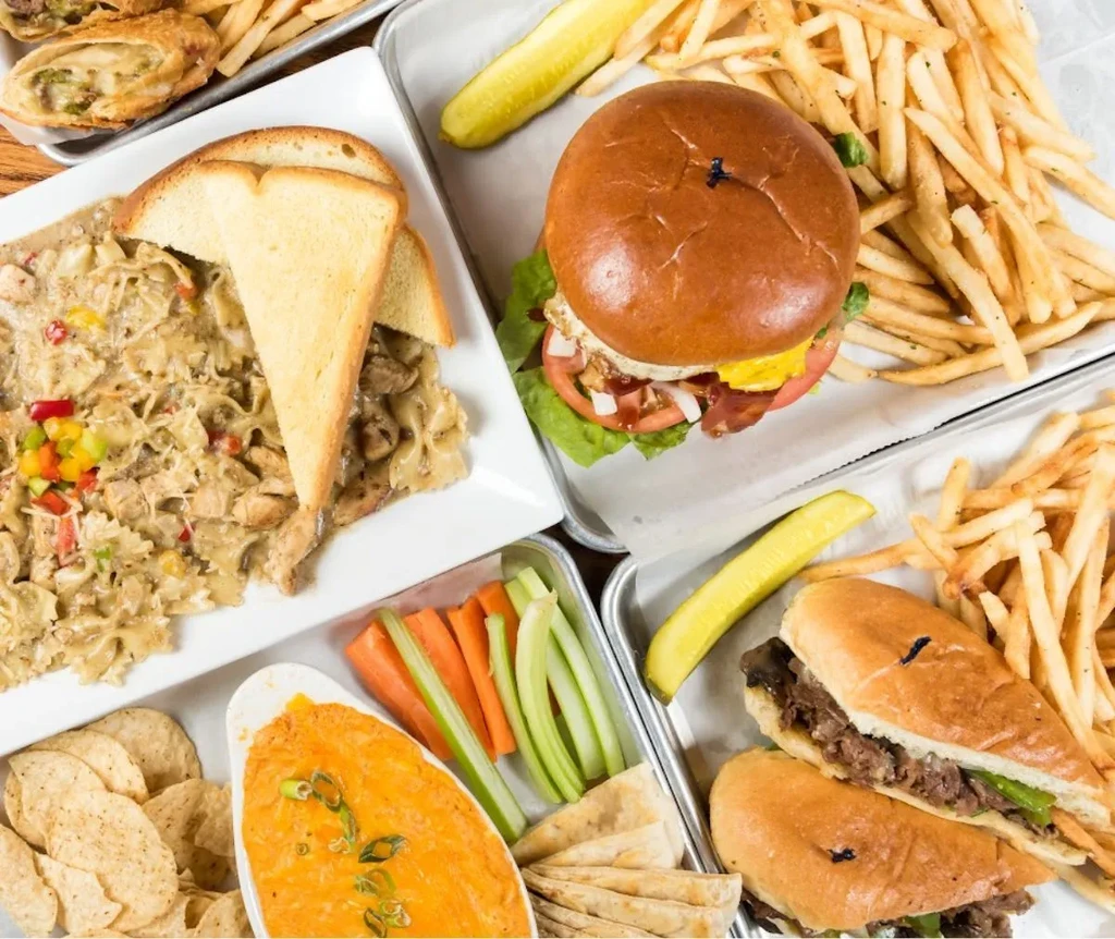 An overhead view of pasta, burger, sub, dip, fries, and vegetables.