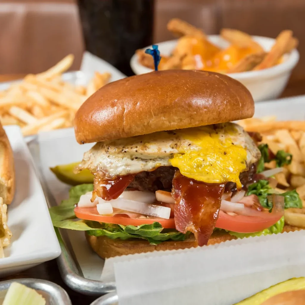 Close-up of a gourmet burger with fried egg, bacon, cheese, and a pickle.