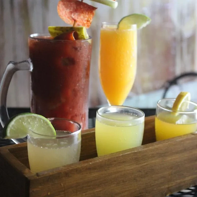 Garnished Bloody Mary, mimosa, and cocktails on a rustic bar table.