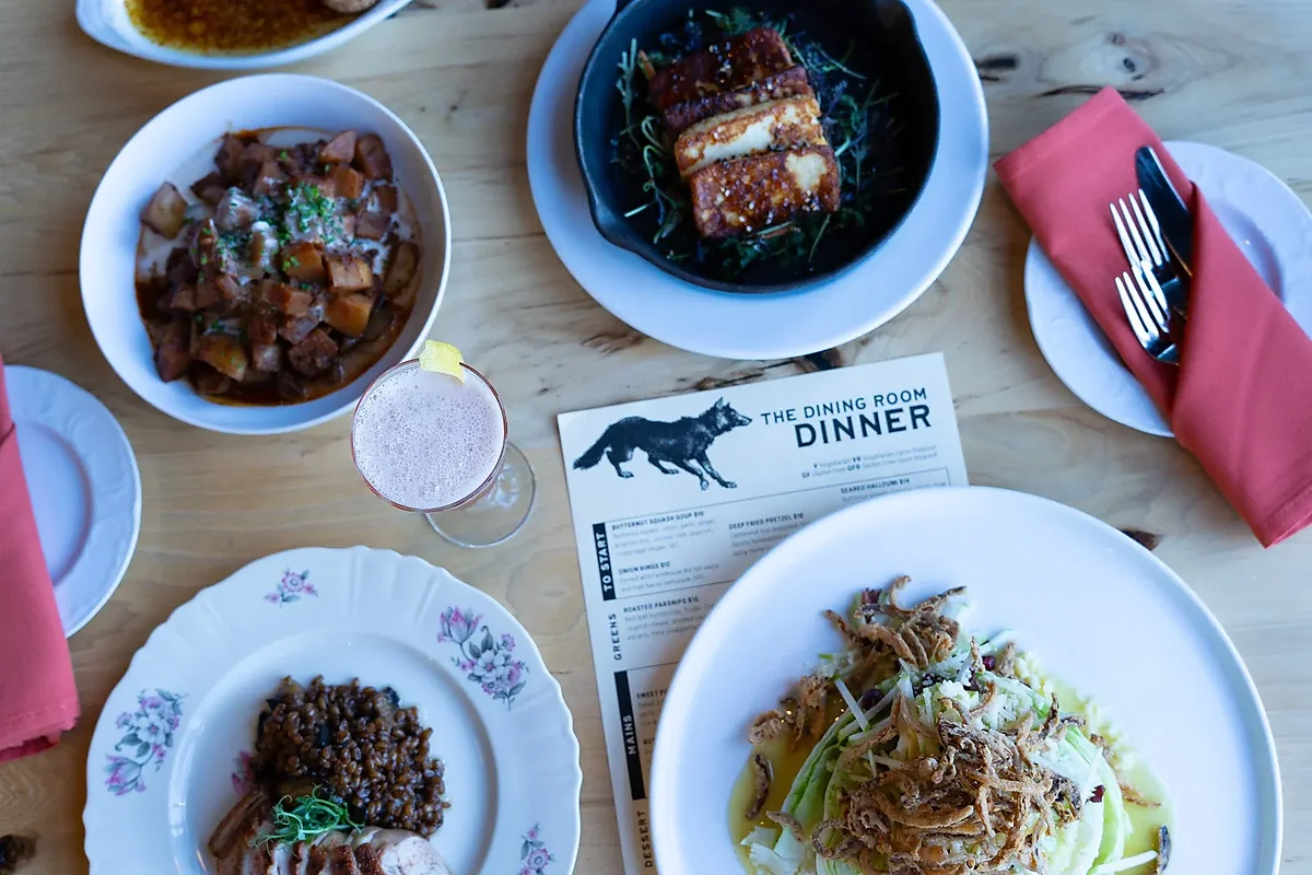 Overhead spread of plated dishes and a cocktail on wood table