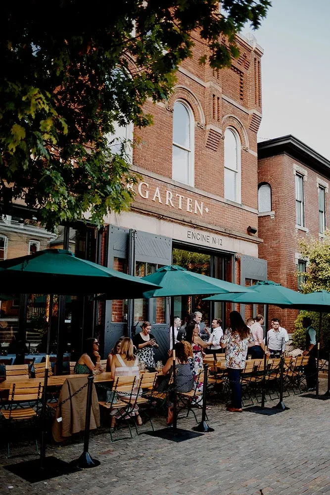 Busy outdoor patio of GARTEN restaurant with many diners and umbrellas.