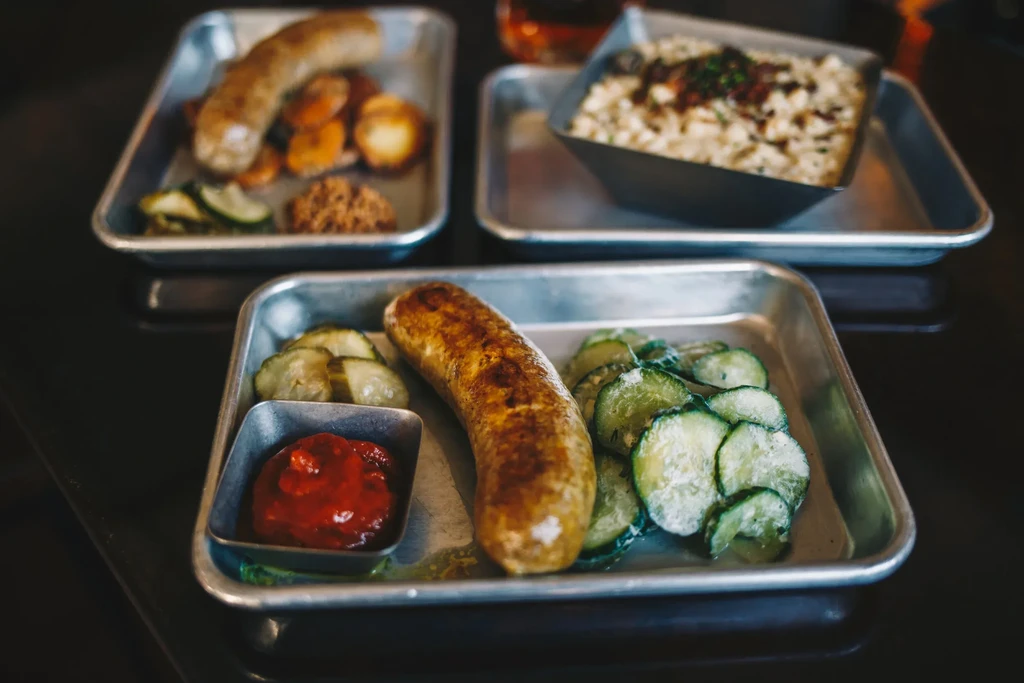 Sausages, pickles, potatoes, and a creamy dish on a dark tabletop.