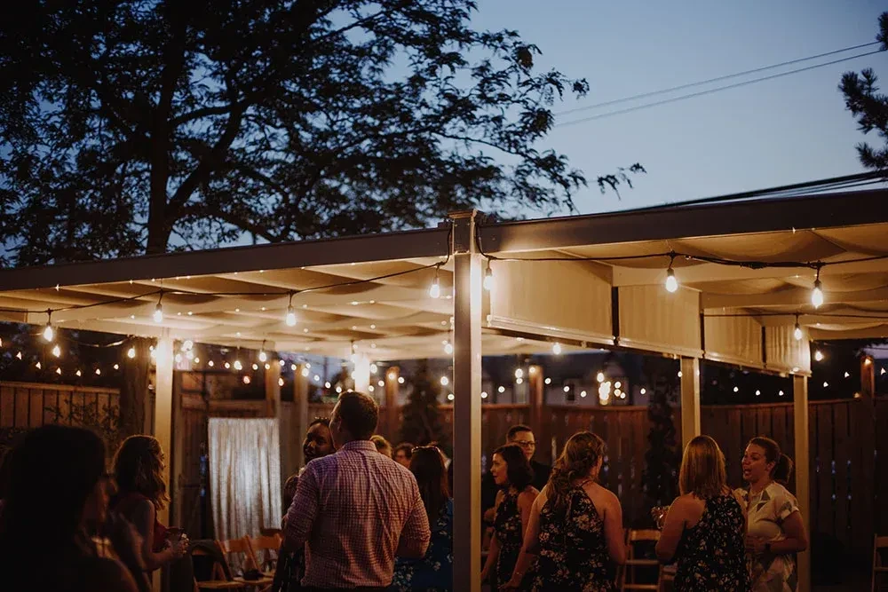 Group socializing outdoors under a canopy of warm string lights.