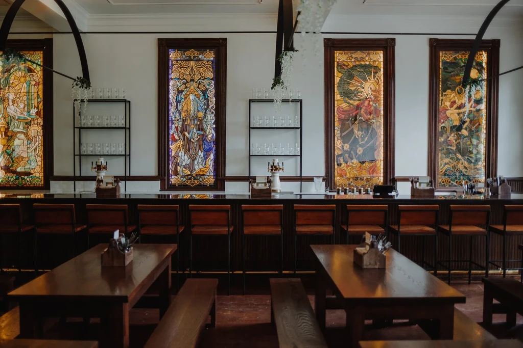 Bar interior featuring colorful stained-glass windows and dark wood furniture.