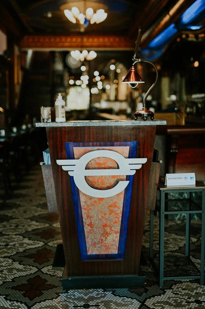 Restaurant host stand with stylized logo, lamp, and hand sanitizer.