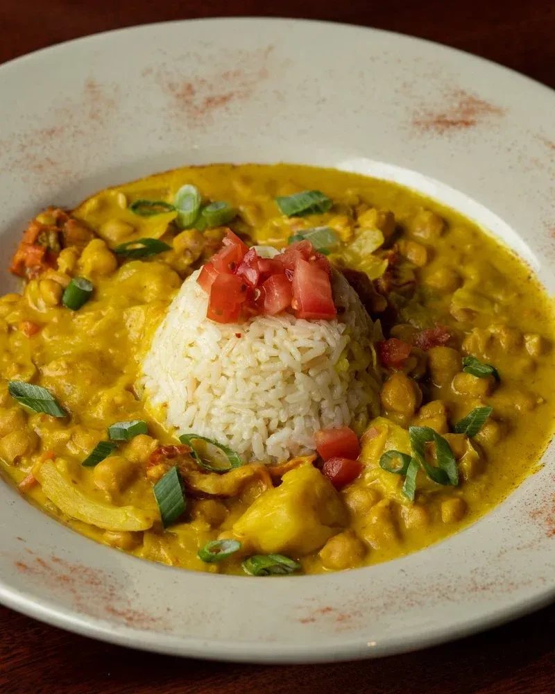 Yellow chickpea curry, white rice, tomatoes, scallions in a white bowl.