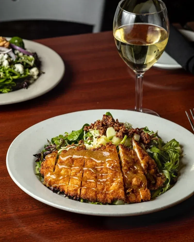 Fried chicken salad with wine on a dark restaurant table.