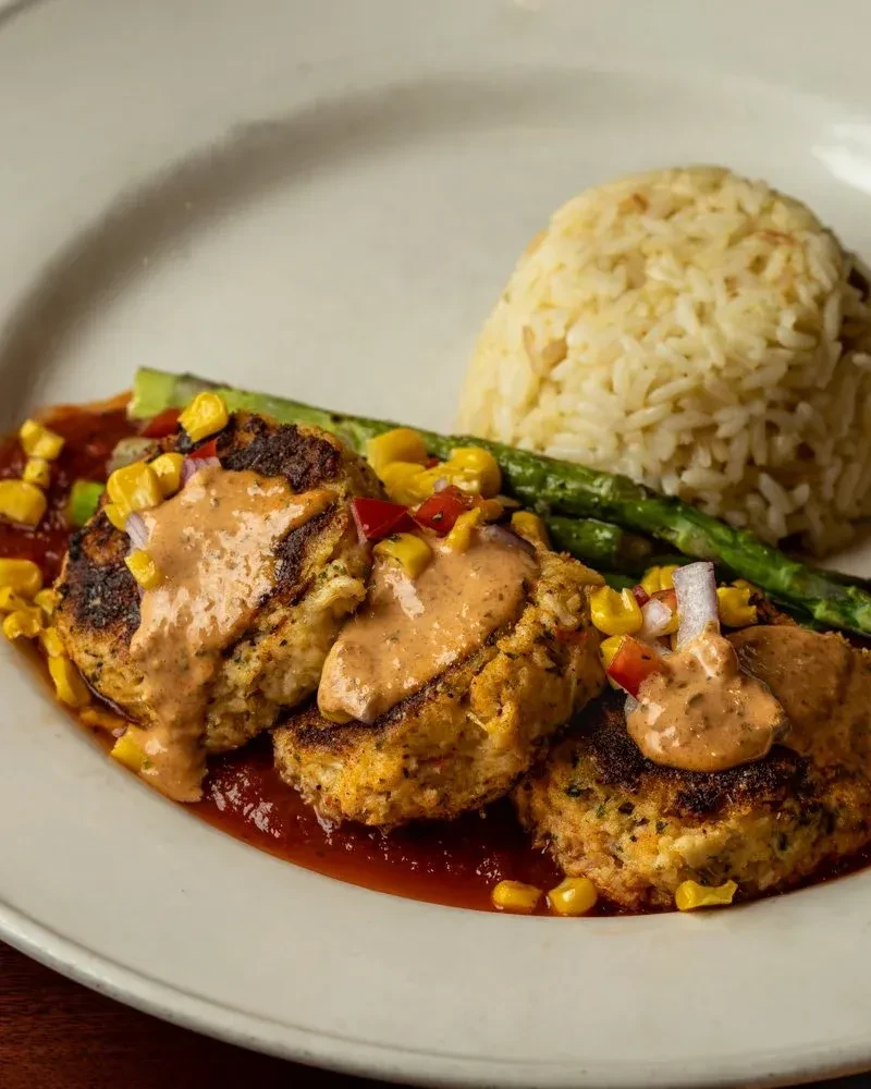 Crab cakes with sauces, corn salsa, white rice, and asparagus.