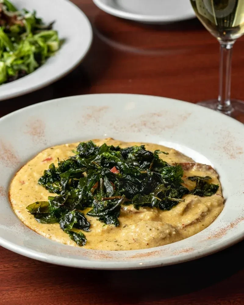 Creamy stew topped with dark green sautéed greens on a white plate.