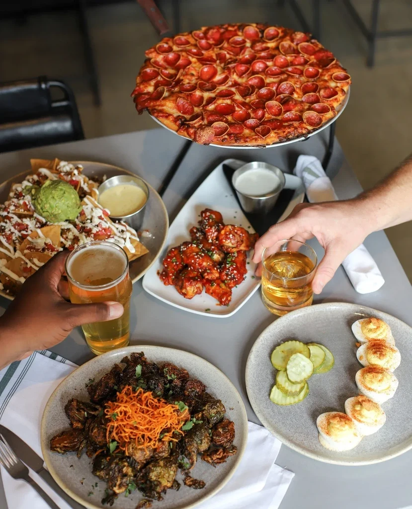 Overhead shot of a restaurant table with pizza, nachos, wings, drinks.