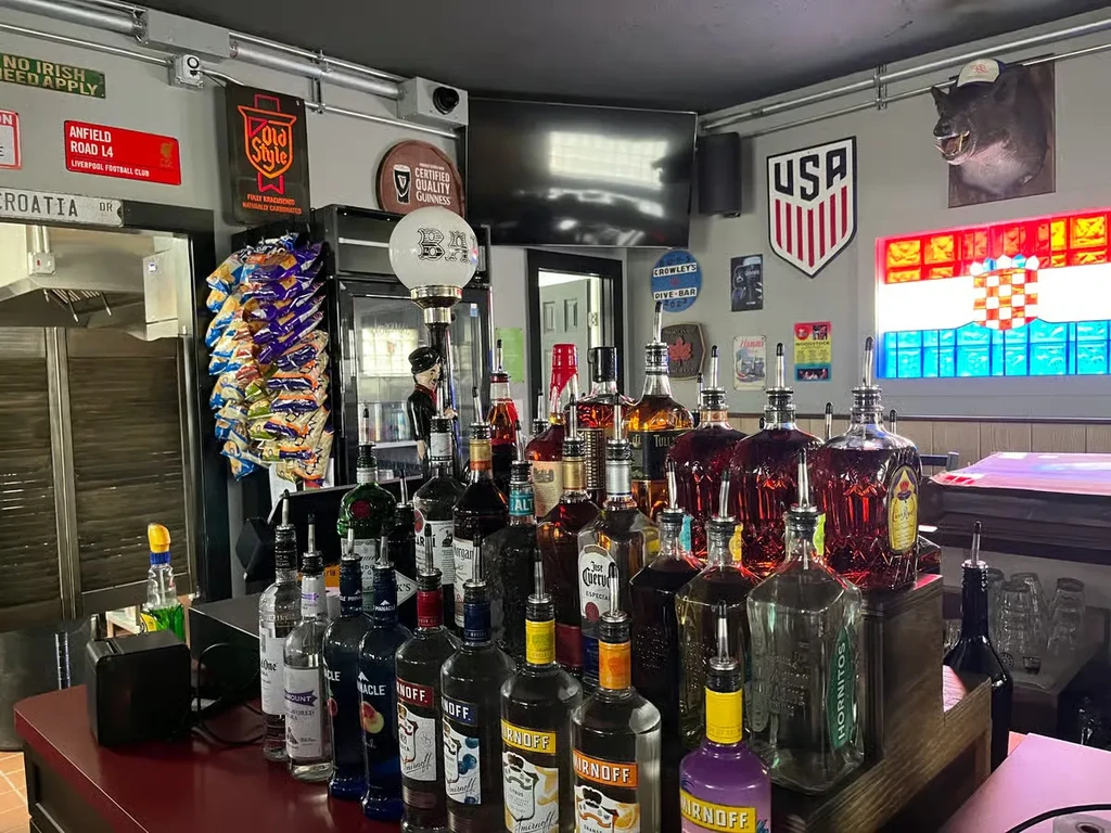 A bar counter filled with liquor bottles and diverse, sports-themed decor.
