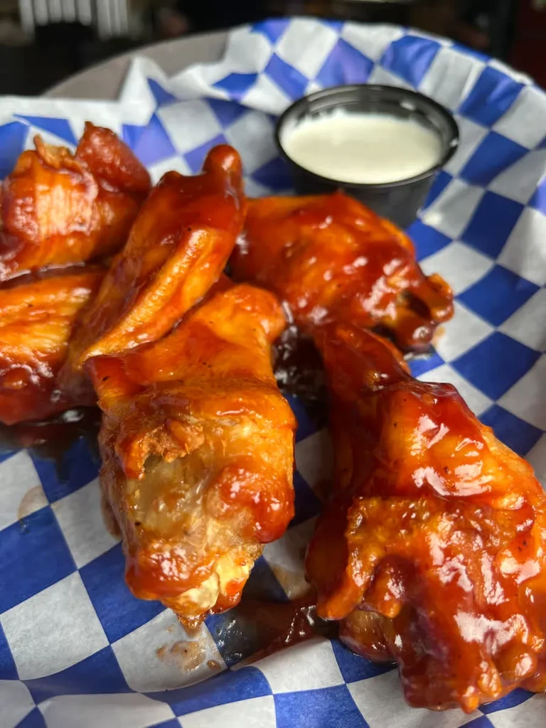 Red-orange sauced chicken wings in a checkered basket with white dip.