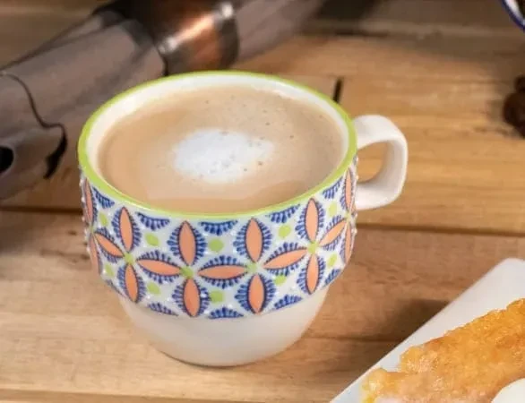 Colorful patterned ceramic mug with frothy coffee and foam.
