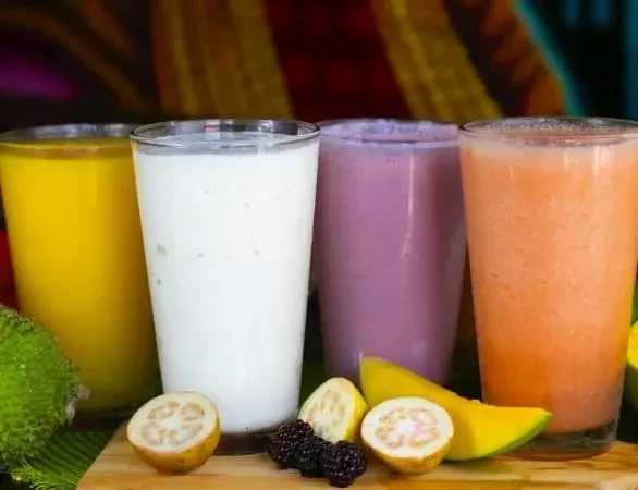 Four colorful beverages and tropical fruits on a wooden board.