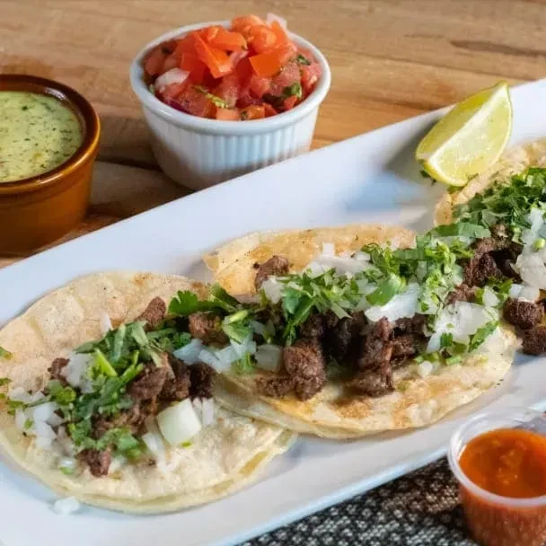 Three street tacos with cilantro, onions, lime, and salsas.
