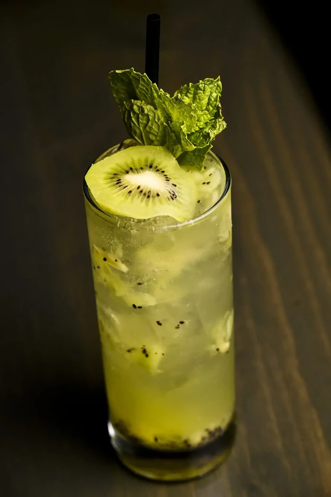 Light green kiwi drink with ice, mint, kiwi slice, and straw.