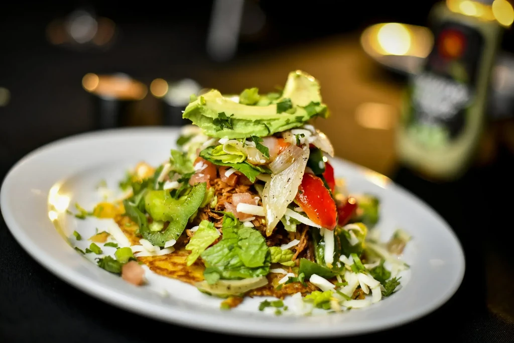 Gourmet taco or tostada with shredded meat, avocado, cheese, and vegetables.