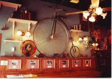 Vintage bar interior with a large penny-farthing bicycle and Budweiser sign.