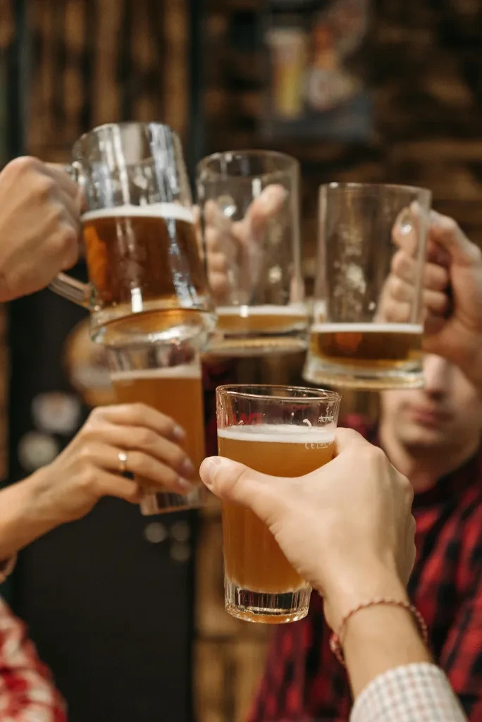 Group toasting with various beer glasses filled with amber beer.