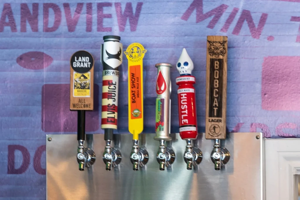 Close-up of six colorful beer taps on a stainless steel draft system.
