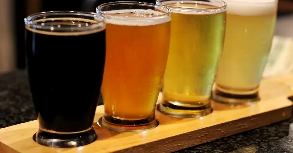 Beer flight with four beers of varying colors on a wooden paddle.
