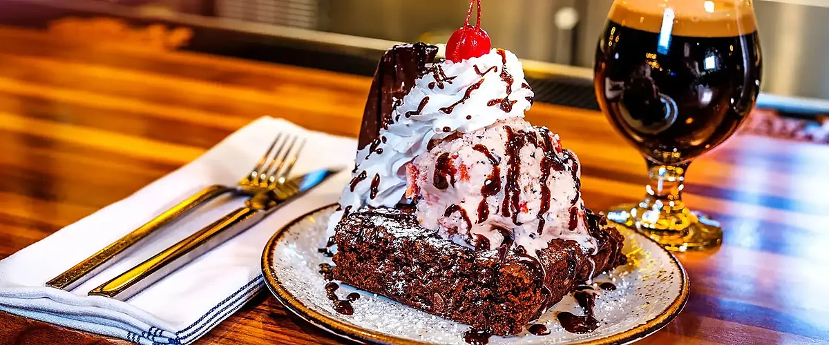 Brownie sundae with whipped cream and cherry next to dark beer