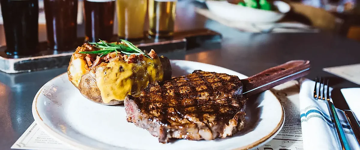 Grilled steak and loaded baked potato beside a beer flight