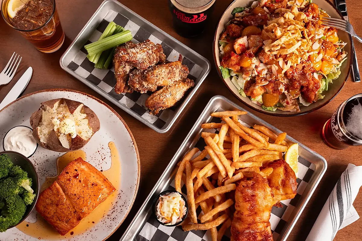 Overhead spread of wings, salad, salmon, fish and fries with beers