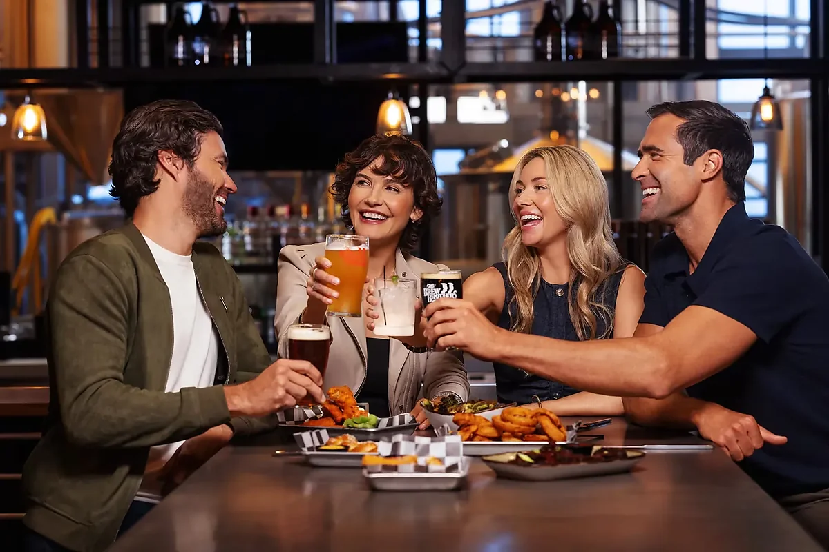 Four guests toasting beers over shared appetizers at the bar